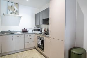 cocina con armarios blancos, fregadero y microondas en Modern and Spacious Apartment in Salford Quays, en Mánchester