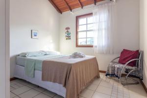 a bedroom with a bed and a chair and a window at Pousada Tehau Guest House in Búzios