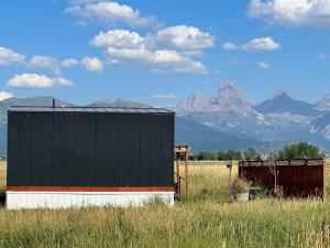 un bâtiment noir dans un champ avec des montagnes en arrière-plan dans l'établissement Teton View Studio - Hidden Gem near Yellowstone, à Tetonia