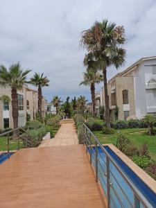 a wooden walkway with palm trees and houses at Les perles de tamaris in Casablanca