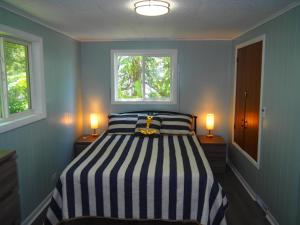 a bedroom with a striped bed with two windows at Cavalier Cottage - Private Lakefront w Kayaks! in Honor