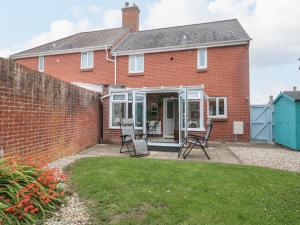 a brick house with chairs on a patio at Pebbles Foxglove Way in Bridport