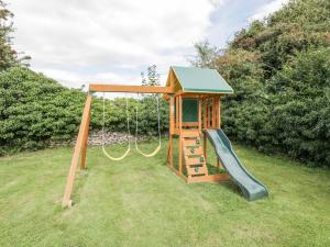 a wooden playground with a slide in a yard at Orchard House Cottage in Malmesbury