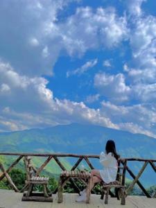 a woman sitting on a bench looking at the mountains at Lù Homestay Tà Xùa in Bắc Yên