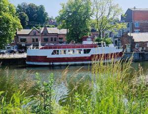 a red and white boat on a river with buildings at Gîte Le Sambre in Thuin