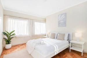 een witte slaapkamer met een wit bed en een plant bij Perfect Manly Retreat. in Sydney