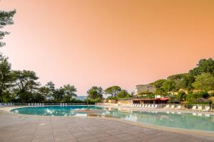 a swimming pool with white chairs and a pink sky at Village Vacances Passion La Bayette in Le Pradet