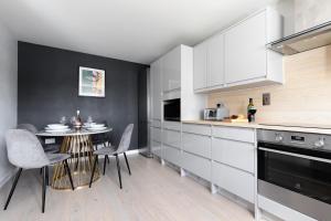 una cocina con armarios blancos y una mesa con sillas. en Unwind in Style - Entire Home with Parking and Stunning Garden, Just Minutes from the Airport!, en Bishops Stortford