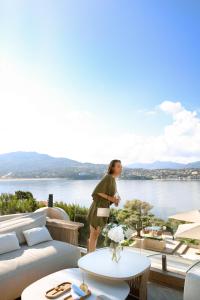 una donna in piedi su un balcone con vista sull'acqua di Hôtel Marinca & Spa a Olmeto