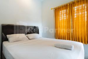 a bedroom with a large white bed with yellow curtains at Teratai Guesthouse at RS Adam Malik Medan Mitra RedDoorz in Medan