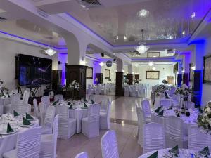 um salão de banquetes com mesas e cadeiras brancas e iluminação roxa em Hotel Turist em Fălticeni