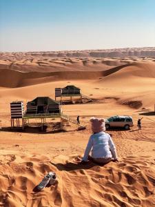 una persona sentada en la arena en el desierto en Oman desert private camp en Shāhiq