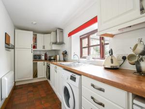 a kitchen with white cabinets and a washer and dryer at Heron Cottage in Colyton