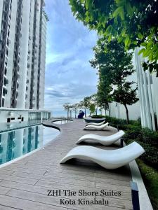 a row of white chairs sitting next to a swimming pool at ZHI The Shore Suites Kota Kinabalu in Kota Kinabalu