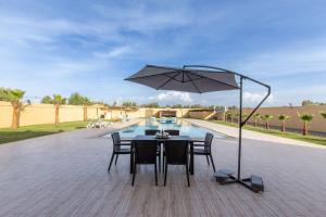 uma mesa com cadeiras e um guarda-sol ao lado de uma piscina em Villa Vista , Piscine 22m , Jeux jardins , Terrain squash em Marraquexe