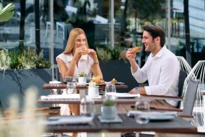 un hombre y una mujer sentados en una mesa comiendo comida en Falkensteiner Hotel Belgrade, en Belgrado