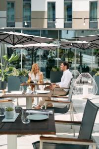 a man and woman sitting at a table under an umbrella at Falkensteiner Hotel Belgrade in Belgrade