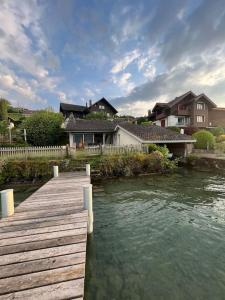 un pont en bois sur une nappe d'eau avec des maisons dans l'établissement NEB-THUN Seehaus Einigen, à Einigen