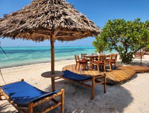 a table and chairs under a straw umbrella on the beach at Almas Beach Boutique Hotel in Makunduchi