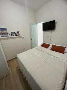 a bedroom with a large white bed with a flat screen tv at Casa Aconchegante com Piscina Barra do Jacuípe in Camaçari