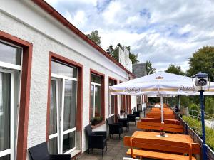 un patio con mesas, sillas y una sombrilla en Pension und Berggasthaus Kapellenstein en Geyer