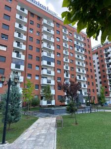 un grand bâtiment en briques rouges avec un parc en face de celui-ci dans l'établissement Modern Apartment, à Ferizaj