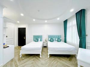 two beds in a white room with blue curtains at Paris Hotel & Cafe in Vĩnh Long