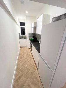 a white kitchen with a refrigerator and a wooden floor at Ground Flr 3-bed flat near Norbury Station in Norbury