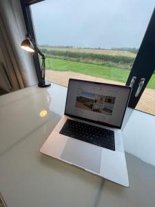 um computador portátil sentado numa mesa de vidro com uma janela em The Meadows 