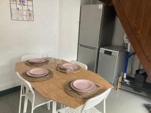 uma mesa de madeira com cadeiras e placas cor-de-rosa e um frigorífico em Charmante petite maison à Olne em Olne