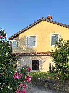 una casa amarilla con flores rosas delante en Quiet countryside apartments near the city and the sea, en Koper