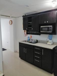 cocina con armarios negros, fregadero y microondas en (2) cuarto maravilloso para descansar y asearse, en Tlaxcalancingo