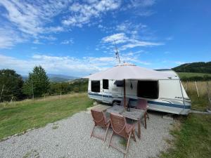 a rv with a table and chairs and an umbrella at Zážitkový pobyt v luxusnom karavane vo Farmárskom Parku in Stožok