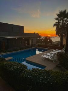 a swimming pool with two lounge chairs and a sunset at Blumen Hotel in Concón