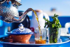 馬拉喀什的住宿－DAR ESSHRA，把一杯饮品倒入玻璃杯的茶壶