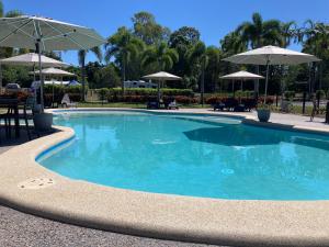 einen Pool mit blauem Wasser und Sonnenschirmen in der Unterkunft Bali Hai Child Free Holiday Park Mission Beach in Mission Beach