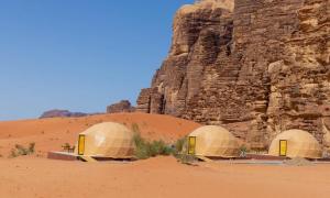 three domes in the desert next to a cliff at Wadi Rum Camp in Wadi Rum