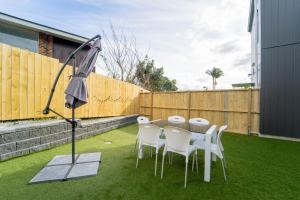 a table with white chairs and an umbrella on the grass at Modern Sunnyhills Town House in Auckland
