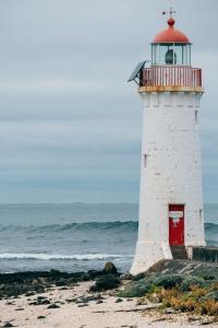 Un faro blanco con una puerta roja en la playa en Nest - charming, comfortable coastal villa, en Port Fairy