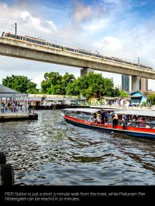 a train on a bridge over a river with two boats at Nasa Bangkok - SHA PLUS Certified in Bangkok