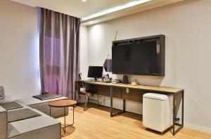 a living room with a desk with a large tv on a wall at Brown Dot Hotel Jeonggwan in Busan