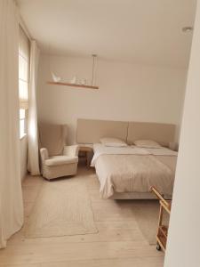 a white bedroom with a bed and a chair at Motyl Apartamenty Studio in Bytom