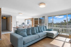 sala de estar con sofá azul y ventanas en Bella Vista: Ocean views a short stroll to beach., en Mollymook