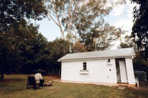 a man sitting in a chair in front of a small building at Pelham Cottage, Kondalilla Falls in Flaxton