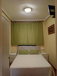 トレドにあるHostal Infantesのベッドルーム(緑のカーテン付きの白いベッド1台付)