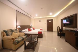 Habitación de hotel con cama, sofá y TV en Hotel Bhagavath Gardens, en Chengannūr