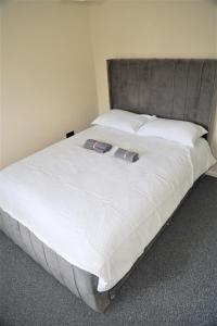 a large bed with white sheets and a gray headboard at Luxe Cosy&Spacious 2 Bed House - Super Fast Wi-Fi & Private Parking Near GLO Airport & Cheltenham Racecourse in Churchdown