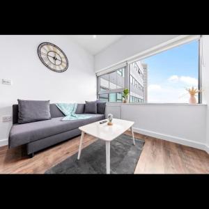 a living room with a couch and a table and a clock at Delta Haven 1 BR Flat 15Mins to LondonBridge DP272 in Croydon