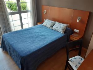 a bedroom with a bed with a blue bedspread and a chair at Pensión Aneira in Puebla de Trives