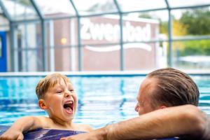 un homme et un garçon dans une piscine dans l'établissement Familie vakantiepark Krieghuusbelten, à Raalte